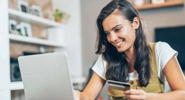 Woman holding credit card while completing an online purchase at home on her laptop