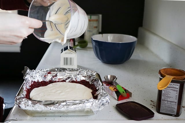 Pouring cheesecake batter over red velvet cake