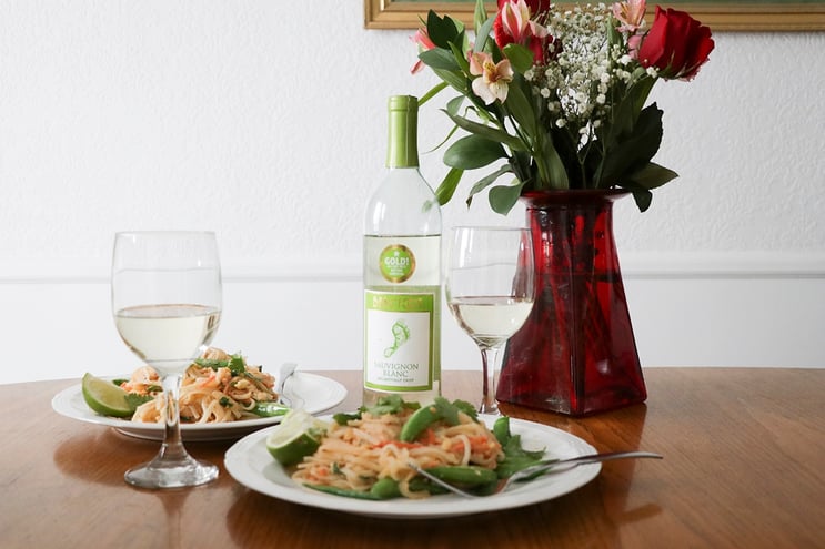 Chicken Pad Thai and Sauvignon Blanc on dining room table by a vase of flowers 