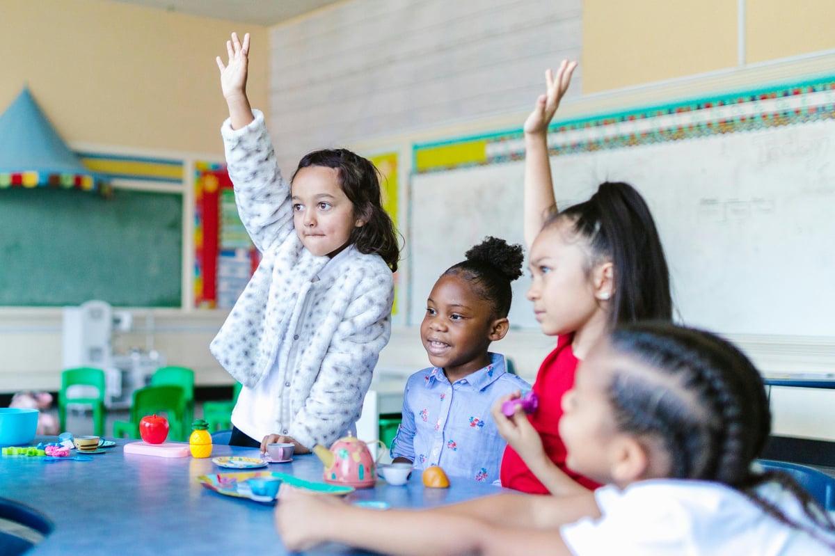 group of young students in a classroom raising their hands
