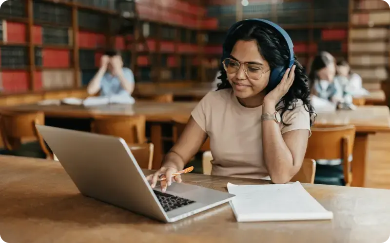 Student with headphones and laptop studying in library